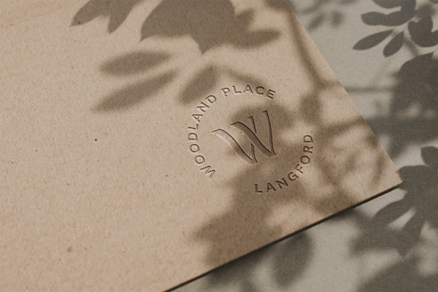 Woodland Place Langford 'W' emblem blind-embossed on kraft paper with leaf shadows