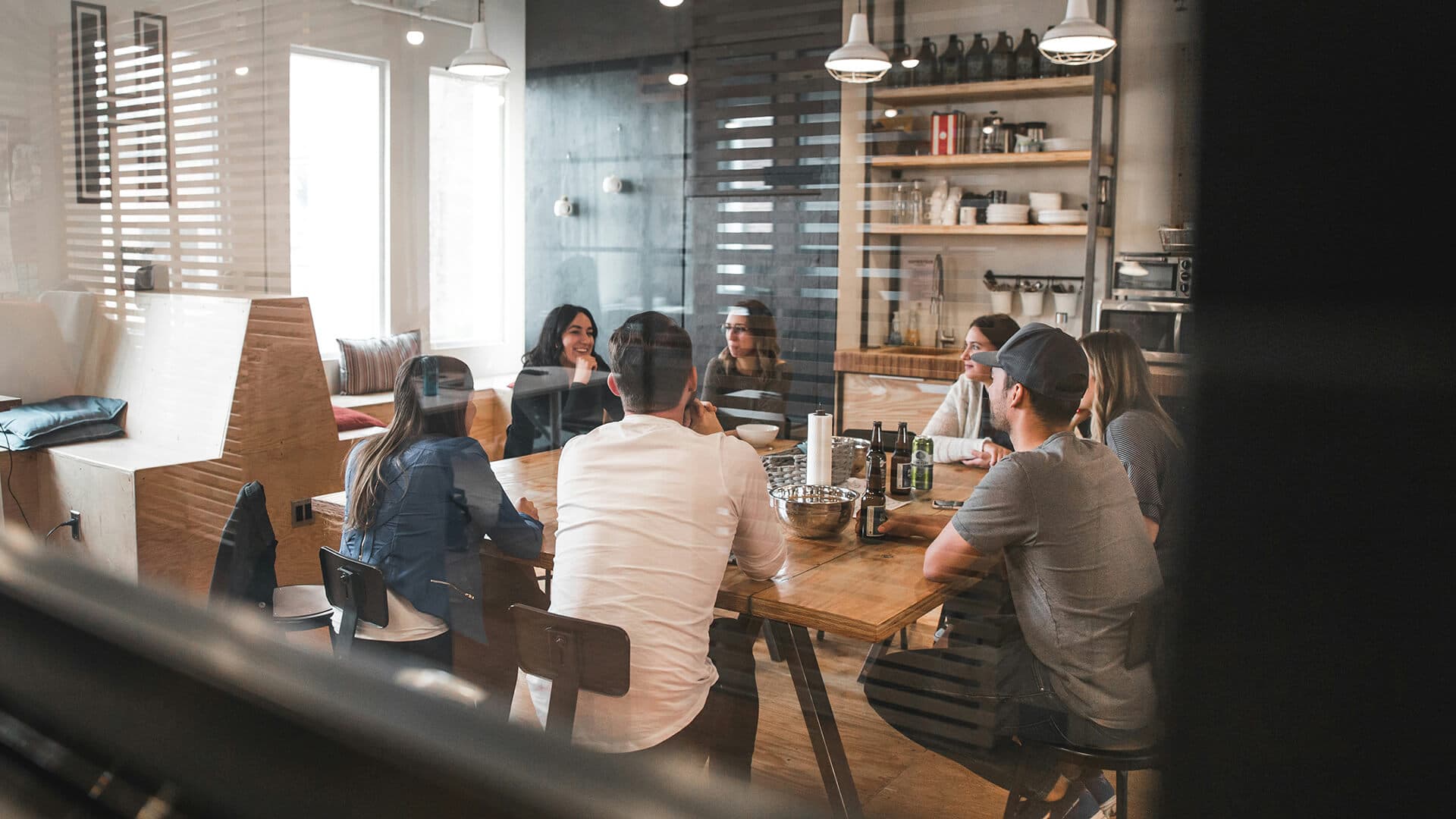 Group of people talking around a wooden table in a bright, casual office kitchen